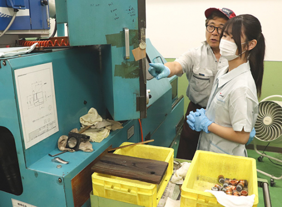 銅の部材を加工する機械の扱い方を教わる生徒（右）＝豊橋市大村町で