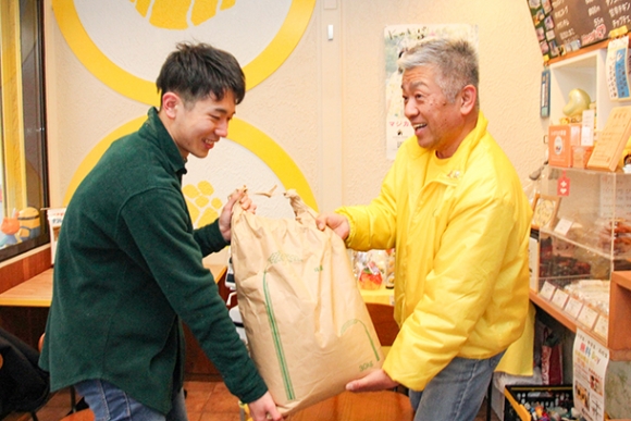 子ども食堂代表の三谷さん（右）にコメを手渡す愛知大の竹内さん＝中村区上石川町３の韓国のり巻き専門店「Ｋのキンパ」で