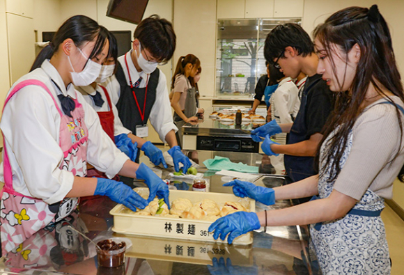 自分たちが商品開発したパンの仕上げをする学生や生徒＝春日井市松本町の中部大で