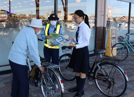 来店客に啓発する三重高自転車競技部の部員ら＝松阪市下村町で