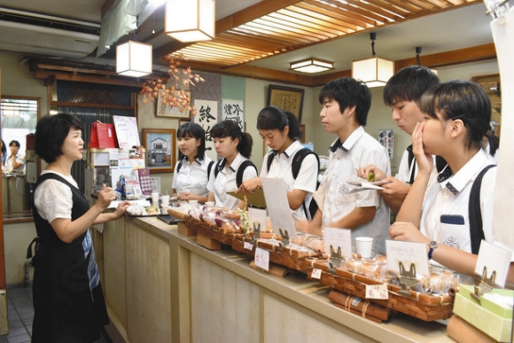 高倉さん(左)から説明を受ける生徒ら=松阪市の鶴の玉たつみ堂で
