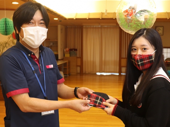 施設長の高橋さん（左）にマスクを手渡す生徒会長の女子生徒＝豊田市大清水町の第２とよた苑で