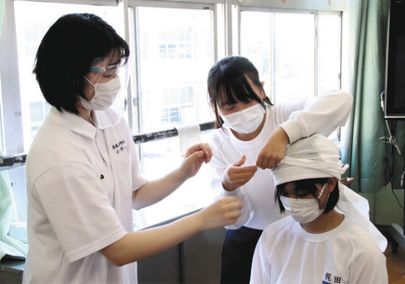 高校生（左）に教わりながら、三角巾を使って頭を保護する中学生＝岐阜市の厚見中で
