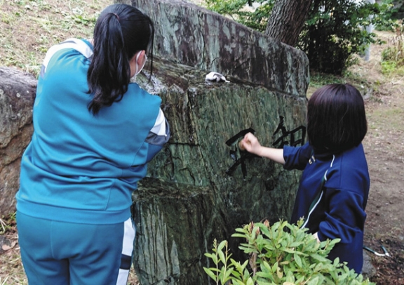 「平和」と書かれた追悼碑を洗う生徒ら＝豊橋市湊町で