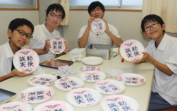 校訓をプリントした瀬戸焼の皿を手に来場を呼びかける部員ら＝東区の東海中学・高校で