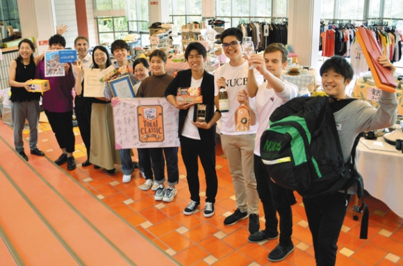 チャリティーバザーで販売する商品を手に来場を呼び掛ける学生たち＝日進市米野木町の名古屋商科大で