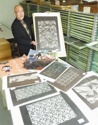染め型紙のコレクションと学生たちが制作したポスターを示す同窓会長の片山さん＝小牧市の名古屋造形大で