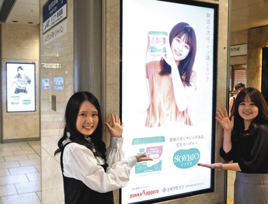 制作した電子看板を前にする金城学院大の学生ら＝ＪＲ名古屋駅で