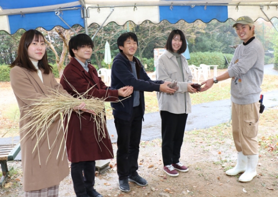 飼育員（右）にサツマイモやドングリを渡す学生たち＝犬山市の日本モンキーセンターで