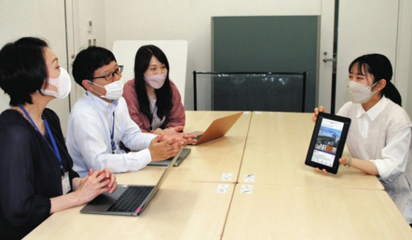 国際センターの大沢優隆事務室長（左から２人目）らに、インスタグラムに投稿する写真について説明する浅井さん（右）＝名古屋市の南山大で