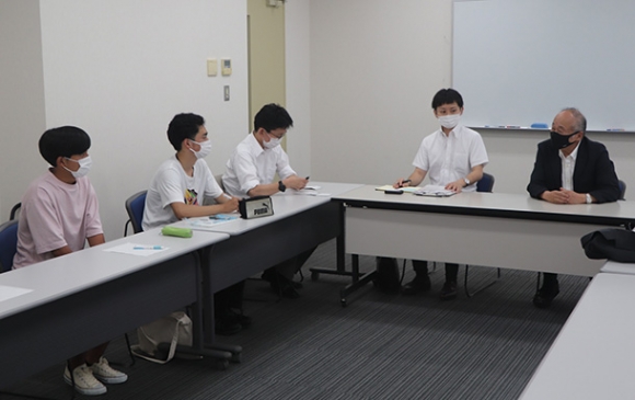 上島さん（右）から事業の説明を受ける学生ら＝伊勢市神田久志本町の皇学館大で