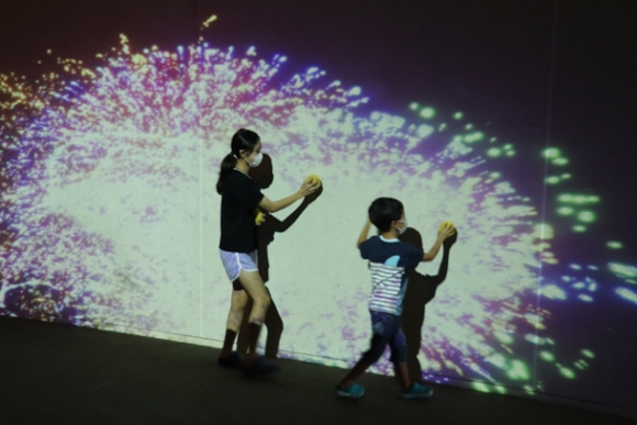 子どもたちが壁にボールをぶつけ、花火を表現したデジタルアートが投影される様子＝武豊町民会館で