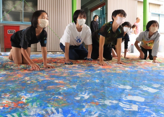 布に手形や足形をつけて楽しむ子どもたちと宇野さん（左から２人目）＝神戸町神戸で
