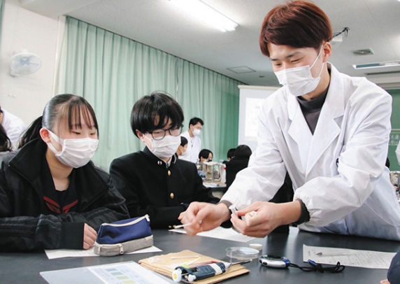 白衣姿の大学生（右）に実験方法を教えてもらう中学生たち＝金沢市高尾台中で