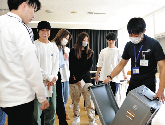 職員が開く投票箱の内側をのぞき込む学生たち＝大府市横根町の至学館大で