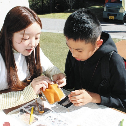 がまぐち作りのワークショップで作り方を教える学生（左）＝豊田市矢並町の鞍ケ池公園で