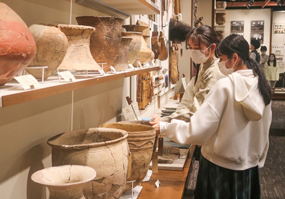 博物館浴の実証実験で、展示品の土器に触れる学生＝昭和区の南山大人類学博物館で