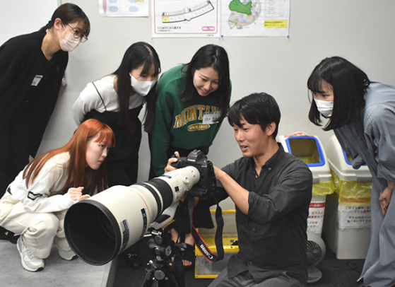 板津記者（右から２人目）からカメラの機能設定などを学ぶ学生たち＝名古屋市昭和区の中京大名古屋キャンパスで