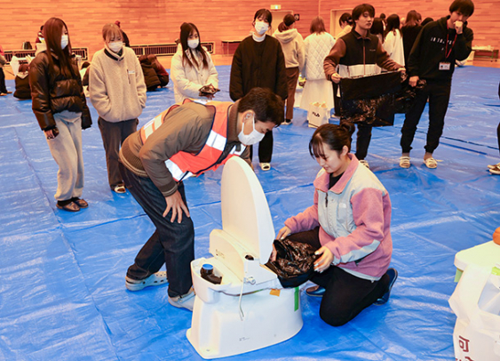 洋式トイレにポリ袋をかぶせる体験をする学生＝可児市虹ケ丘の岐阜医療科学大可児キャンパスで