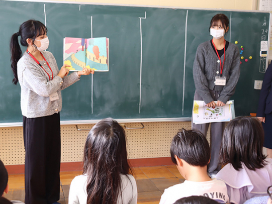 給食の時間の前に、ニンジンが登場する絵本を児童に読み聞かせる名古屋経営短大生＝尾張旭市南新町の本地原小で