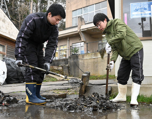 側溝にたまった泥をかき出す学生＝輪島市深見町で