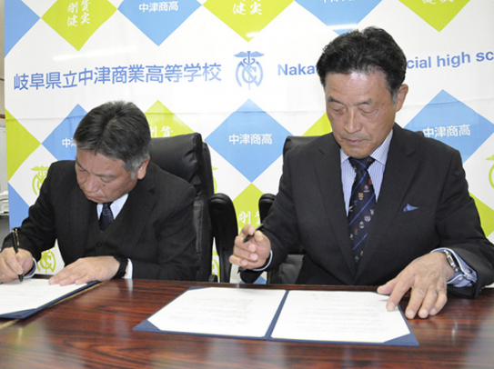協定書にサインする丸山校長（左）と石川学長＝中津川市の中津商業高で