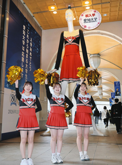 大学に向かう新入生らにエールを送る応援団チアリーディング部とナナちゃん人形＝名古屋・名駅で