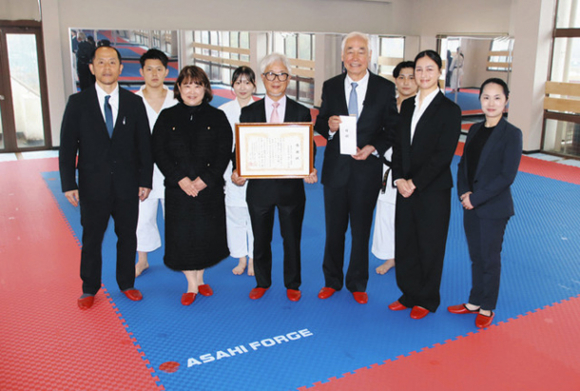 マットを贈った朝日社長（前列左から３人目）と本島学長（同４人目）＝関市桐ケ丘の中部学院大で