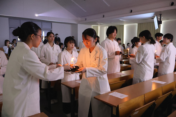 ろうそくの明かりをつなぐ学生たち＝四日市市の四日市看護医療大で