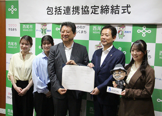 協定書を手にする中村市長（右から２人目）と広瀬学長（同３人目）。学生が持つぬいぐるみは愛知大創業者を模したキャラクターＫＩＩＣＨＩ（キイチ）くん＝西尾市役所で