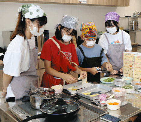 学生に見守られながら調理する子どもたち＝日進市のマチテラス日進で