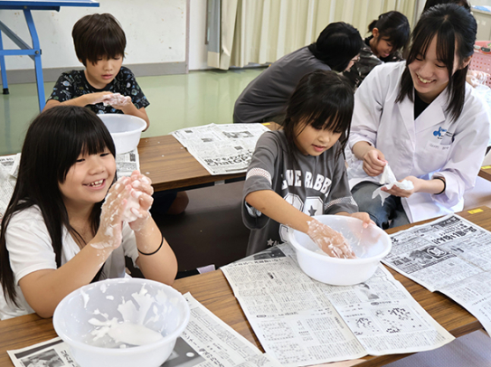 大学生（右）の手ほどきを受けながら科学実験を楽しむ児童たち＝米原市杉沢で