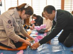 西部さん（右）らの指導でしないに和紙の花を付けていく学生たち＝美濃市中央公民館で