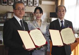 協定書に調印した竹本学長(右)と鈴木校長(左)。中央はまほろばさん=名古屋市西区の名古屋西高で