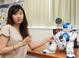 実験に使う人型ロボットを前に「自閉症児のロボットセラピーは有効」と話すイさん＝春日井市の中部大で