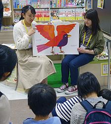 カラフルな動物が登場する英語の絵本で、読み聞かせをする学生たち＝日進市赤池町で