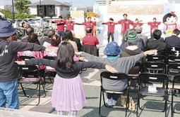 ステージ上の岐阜経済大の学生らの振り付けに合わせて体を動かす来場者たち＝大垣市奥の細道むすびの地記念館で