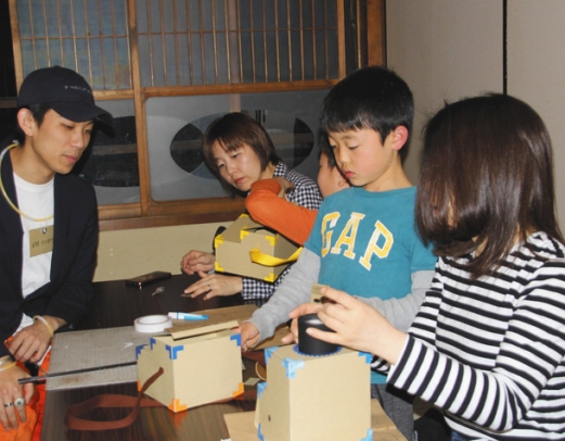 学生の説明を受けながらスマホ映写機を作る子どもたち＝半田市亀崎町の街かどサロンかめともで
