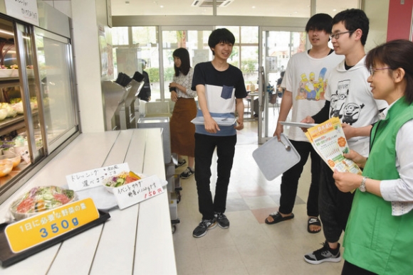 学生らに野菜摂取を呼び掛ける保健所職員（右）＝１９日、関市の中部学院大関キャンパスで